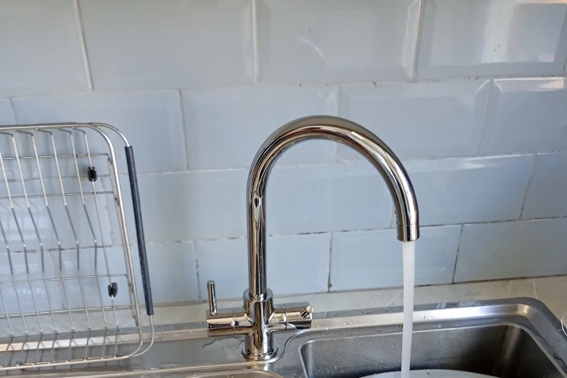 Chrome kitchen mixer tap running into a stainless steel sink